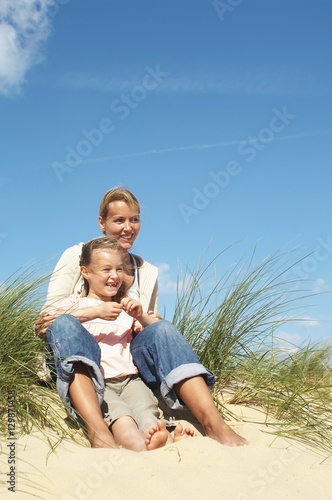 Happy mother and little daughter sitting on sand at beach