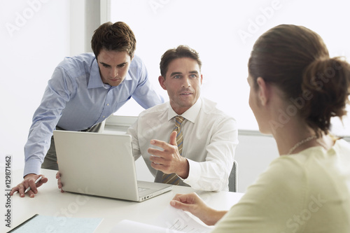 Businessman discussing with colleagues while working on laptop at desk in boardroom