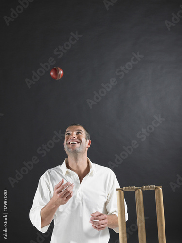 Foto Happy young cricket player tossing ball in the air by stumps against black backg