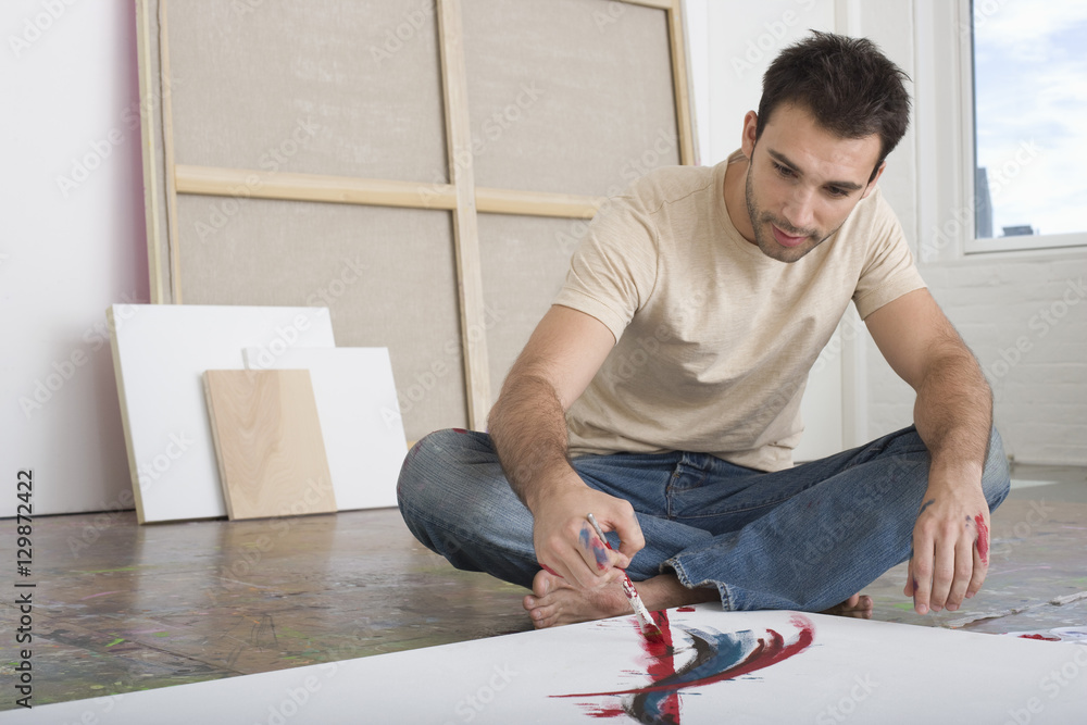 Young man painting on canvas on studio floor Young man painting on canvas on studio floor