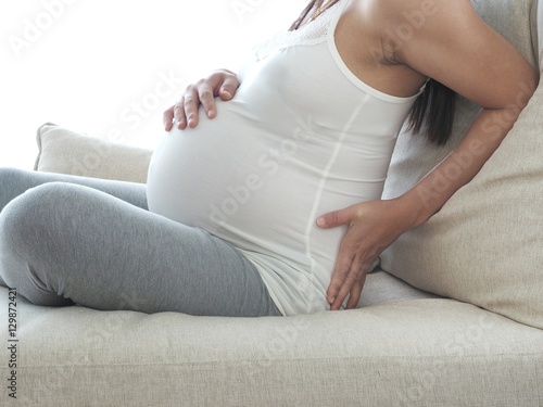 Pregnant woman with painful back on the sofa. Concept of pregnancy healthcare.