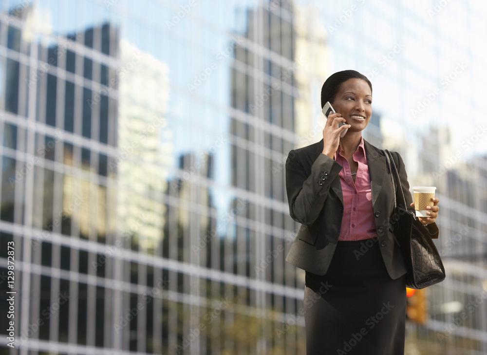 Smiling African American businesswoman using mobile phone on street against building Smiling African American businesswoman using mobile phone on street against building