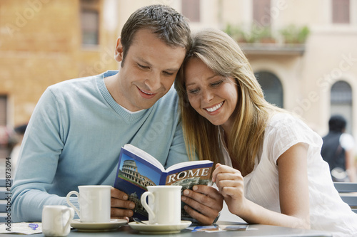 Φωτογραφία Smiling young couple at outdoor cafe looking at guidebook of Rome