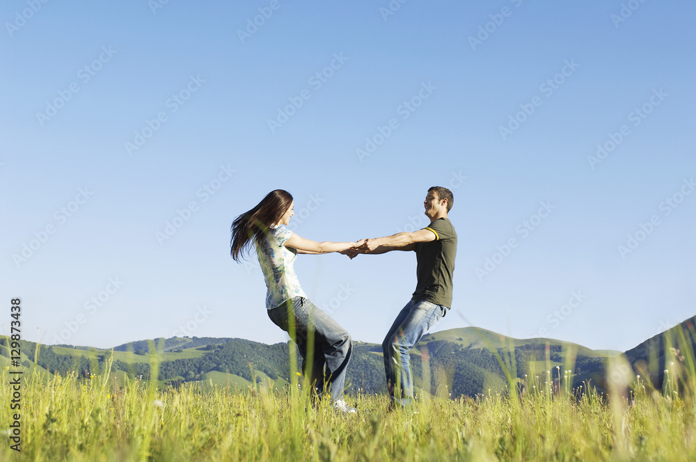 Side view of young loving couple playing against mountain range and clear sky at park Side view of young loving couple playing against mountain range and clear sky at park