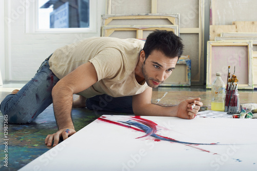 Εκτύπωση καμβά Young male artist looking at canvas on studio floor