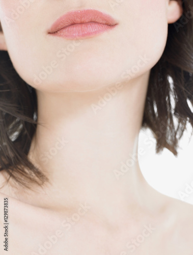 Closeup of young woman's pink lips and neck against white background