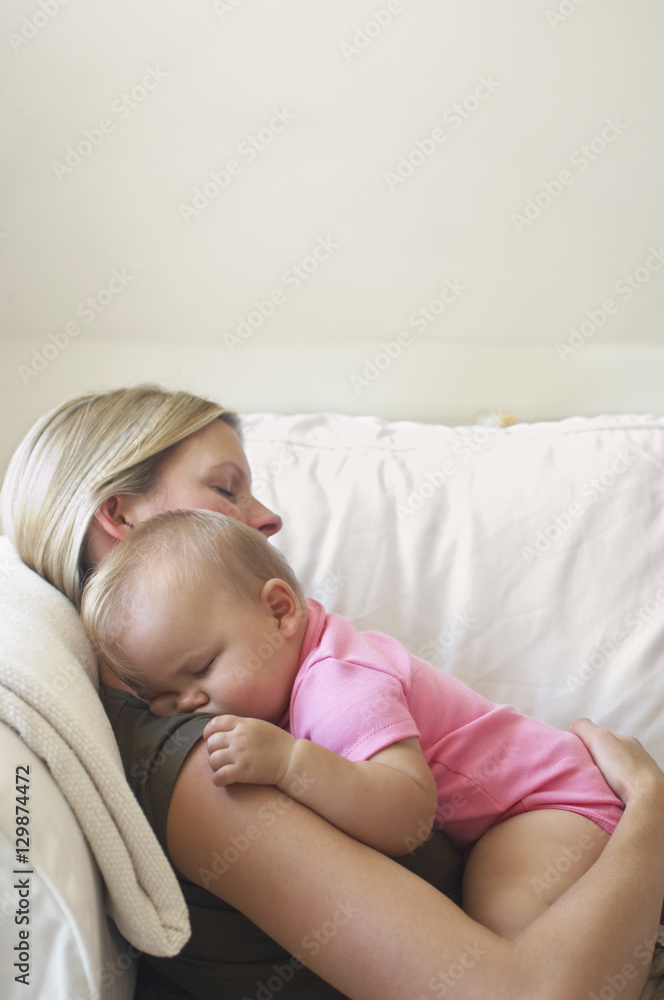 Side view of a young mother with baby sleeping on sofa at home Side view of a young mother with baby sleeping on sofa at home