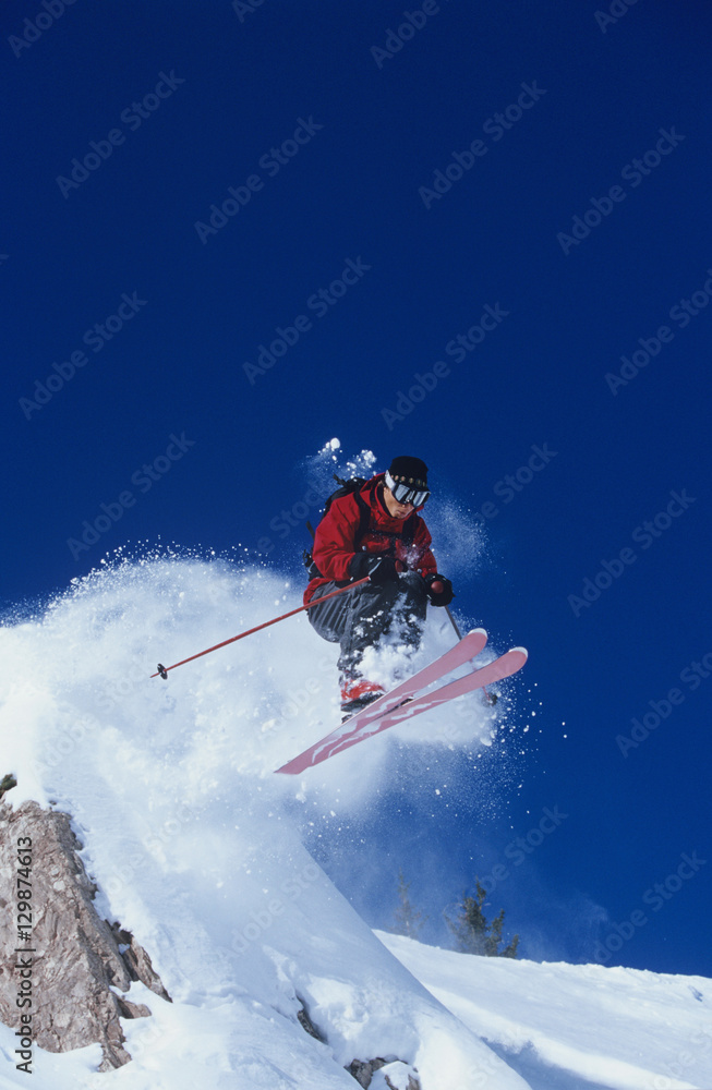 Full length of skier jumping from mountain ledge with deep blue sky in background