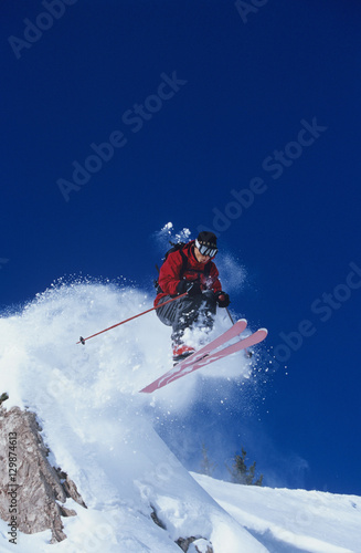 Full length of skier jumping from mountain ledge with deep blue sky in background