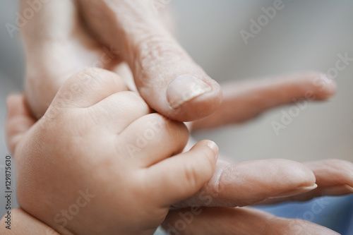 Closeup of a baby holding aged person's hand against blurred background