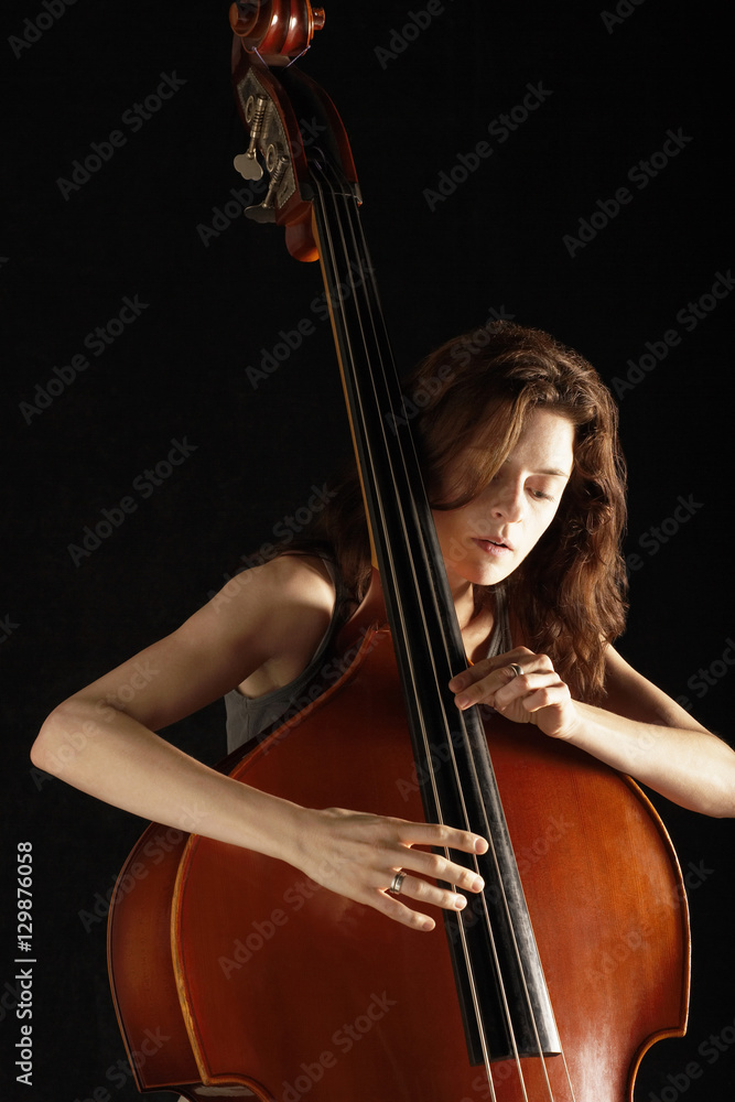 Young woman playing double bass against black background Young woman playing double bass against black background