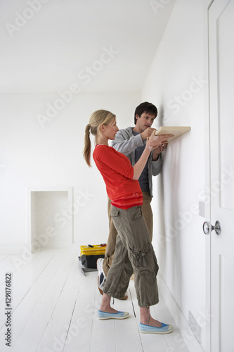Side view of a couple putting up shelf in their new home © moodboard