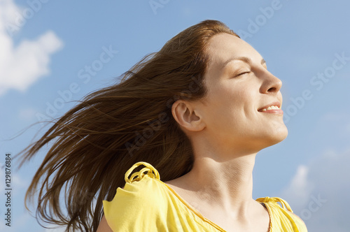 Closeup of young woman with eyes closed enjoying sunlight against sky