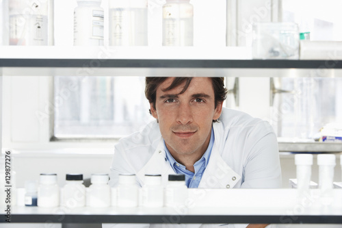 Portrait of confident male scientist looking through shelves in laboratory