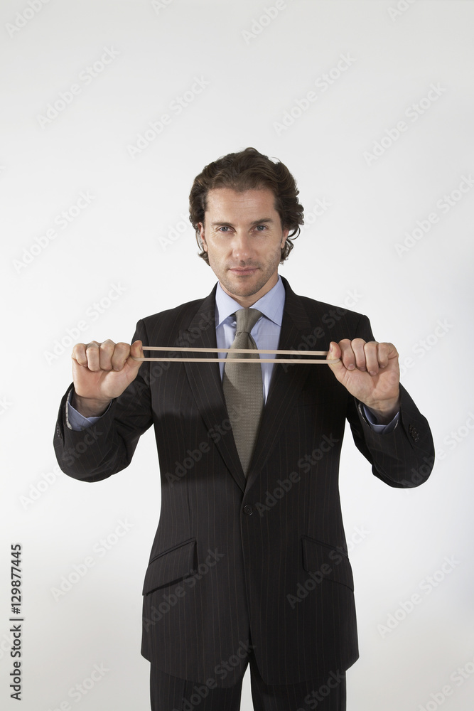 Portrait of a businessman stretching rubber band on gray background Portrait of a businessman stretching rubber band on gray background