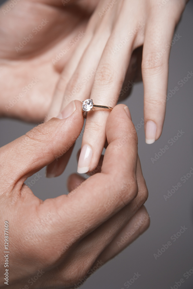 Closeup of man placing engagement ring in woman's finger against gray background Closeup of man placing engagement ring in woman's finger against gray background