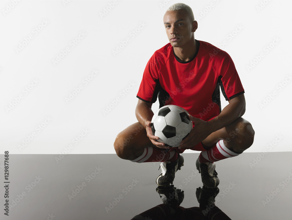Portrait of a player squatting with football in hands against white background Portrait of a player squatting with football in hands against white background