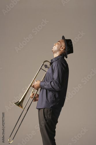 Side view of a happy African American man with trombone standing against brown background photo
