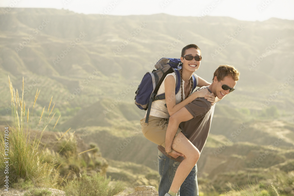 Young man giving piggyback ride to woman while hiking through mountains