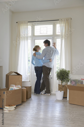 Rear view of a couple standing by window surrounded by boxes © moodboard