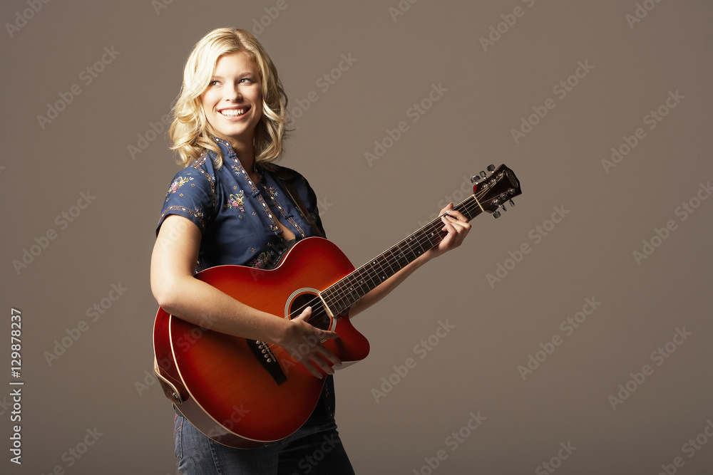 Happy young woman playing guitar against brown background Happy young woman playing guitar against brown background