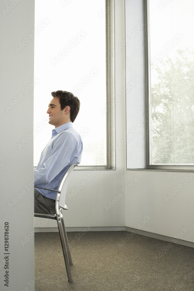Profile shot of young businessman sitting on chair in office Profile shot of young businessman sitting on chair in office