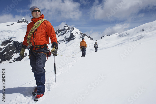 Three male hikers joined by safety line on snowy mountains