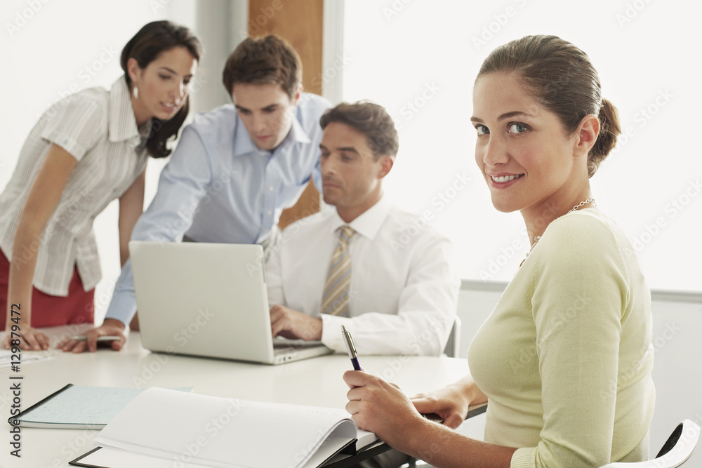 Portrait of beautiful young businesswoman sitting with colleagues working on laptop at desk in office