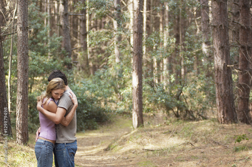 Side view of a couple standing on forest trail and hugging