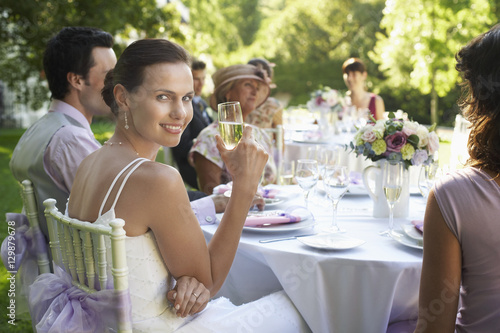 Photography Portrait of beautiful bride holding champagne flute while sitting with guests at