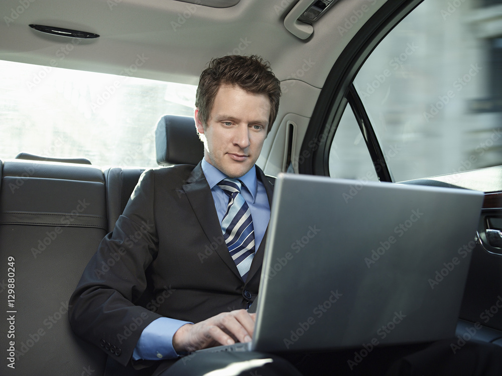 Young businessman using laptop in back seat of car