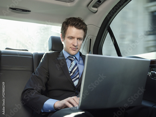 Young businessman using laptop in back seat of car © moodboard