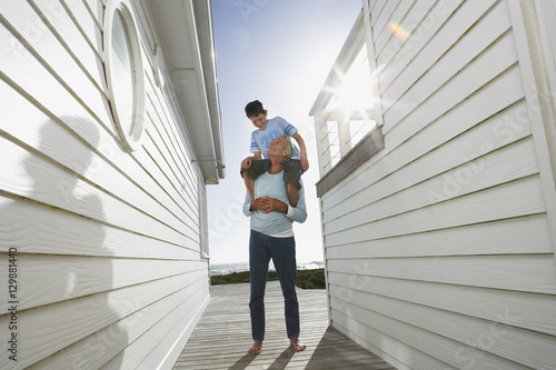 Foto Full length of grandfather carrying grandson on shoulders between beach houses