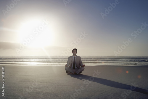 Full length of young businessman meditating in lotus position on beach