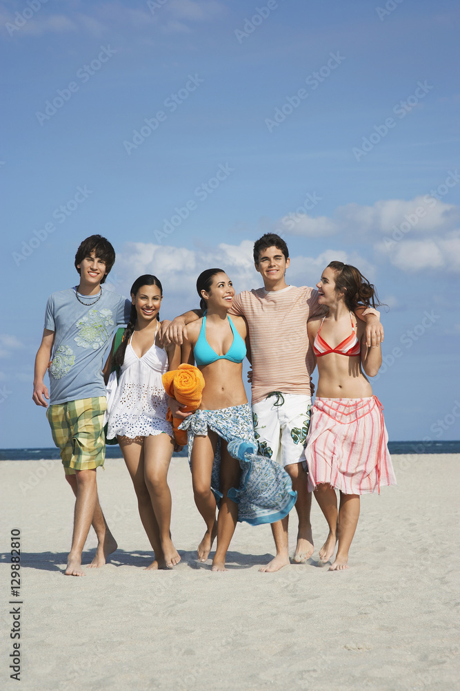 Full length of happy teenage friends walking together on sandy beach