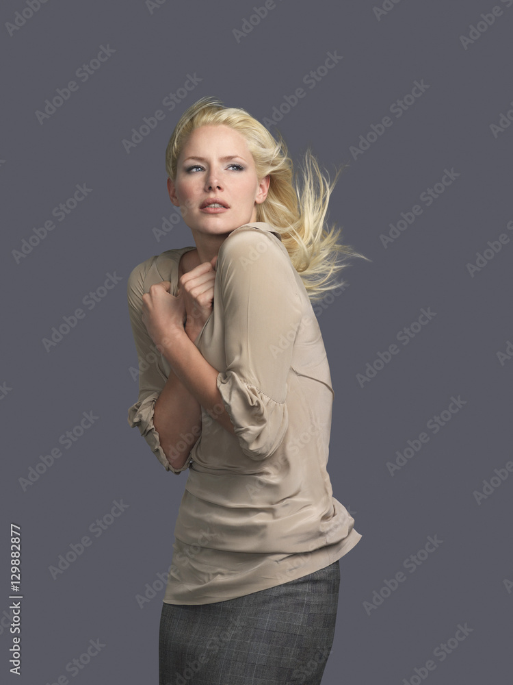 Beautiful young blond woman with hair blowing and arms crossed against gray background Beautiful young blond woman with hair blowing and arms crossed against gray background