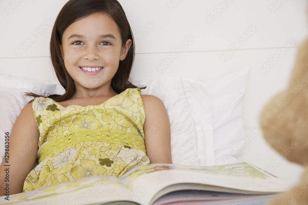 Portrait of happy girl reading story book to her teddy bear in bed Portrait of happy girl reading story book to her teddy bear in bed