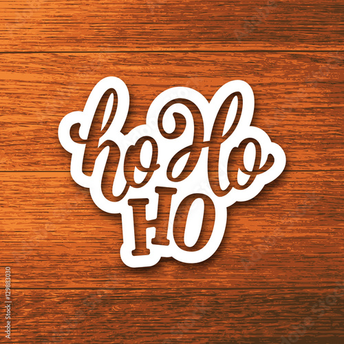 Ho-ho-ho text on white paper label with hand lettering over wooden background. Vector sticker design for Christmas and New Year decoration