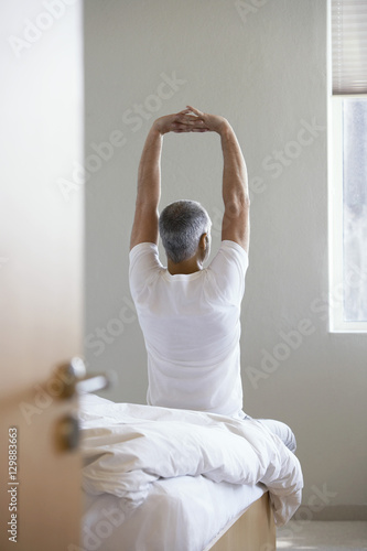 Εκτύπωση καμβά Rear view of middle aged man stretching hands while sitting on edge of bed