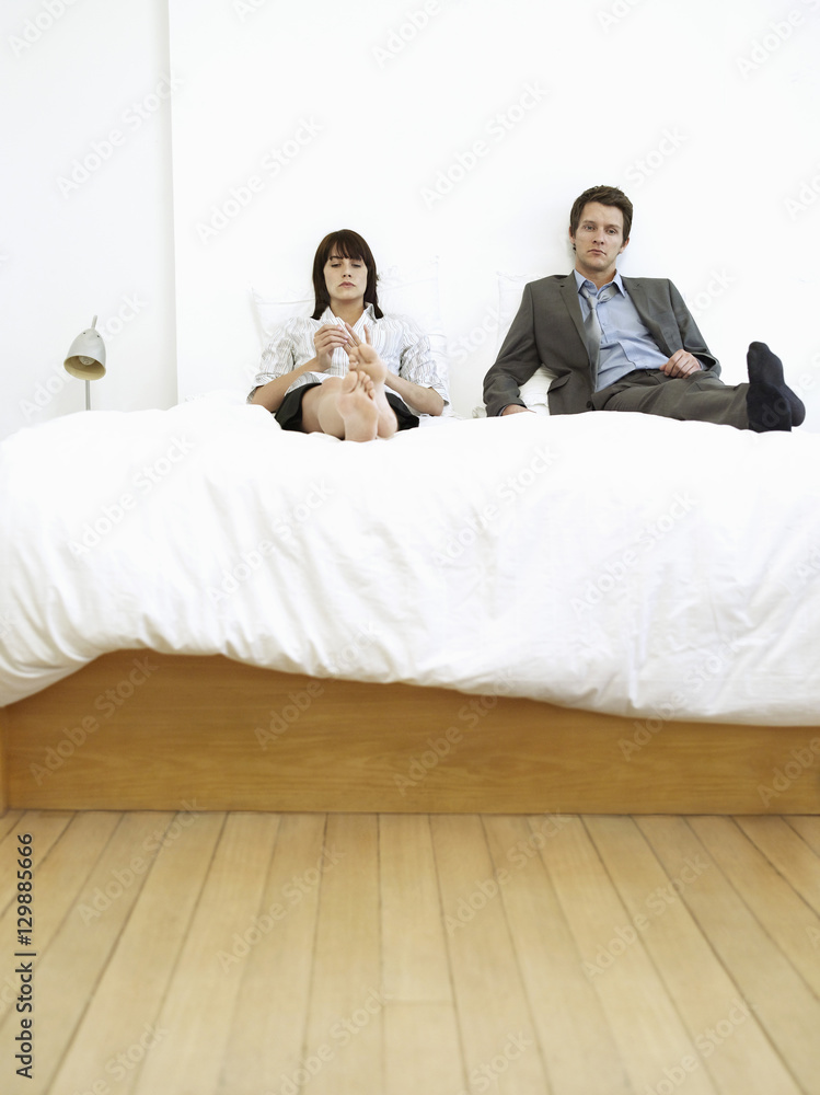 Young business couple sitting on bed, ignoring
