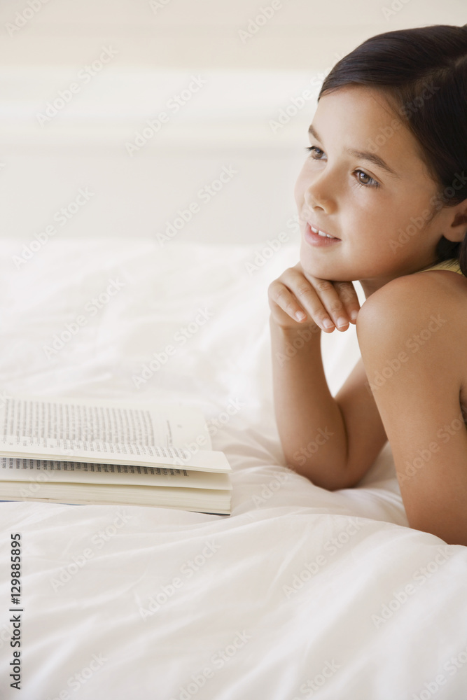 Obraz premium Happy little girl daydreaming while reading story book in bed