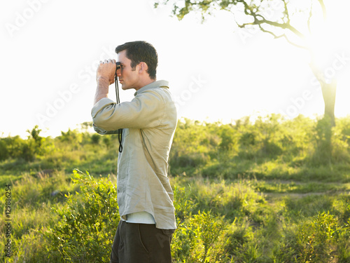 Side view of a man looking through binoculars in field