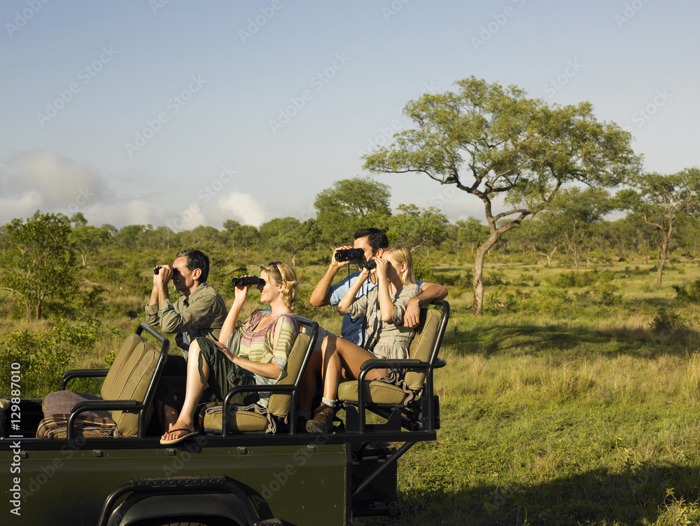 Group of tourists sitting in jeep and looking through binoculars