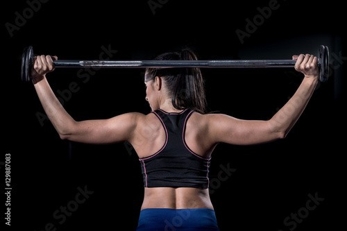 Woman bodybuilder lifting barbell isolated over black background