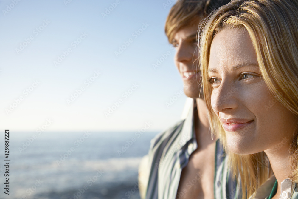 Closeup of happy young woman with man in background by ocean Closeup of happy young woman with man in background by ocean
