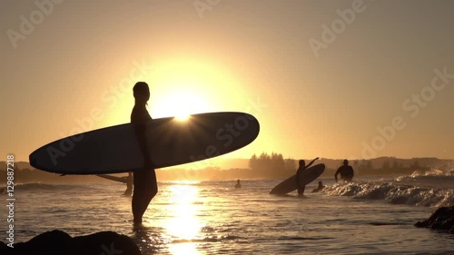 SLOW MOTION: Young woman surfer holding longboard, pointing into beautiful sea