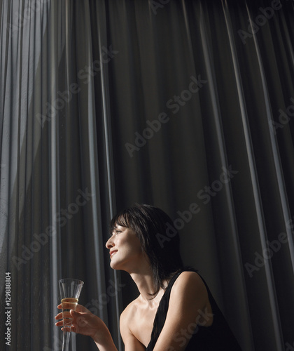 Beautiful young woman drinking champagne in front of curtains