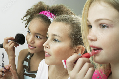 Obraz na plátně Closeup side view of three girls side by side putting on makeup and lipgloss