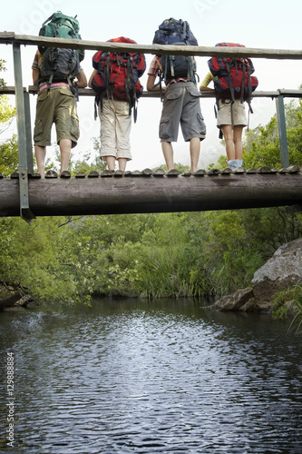 Rear view of teenage boys and girls carrying backpacks on bridge looking down