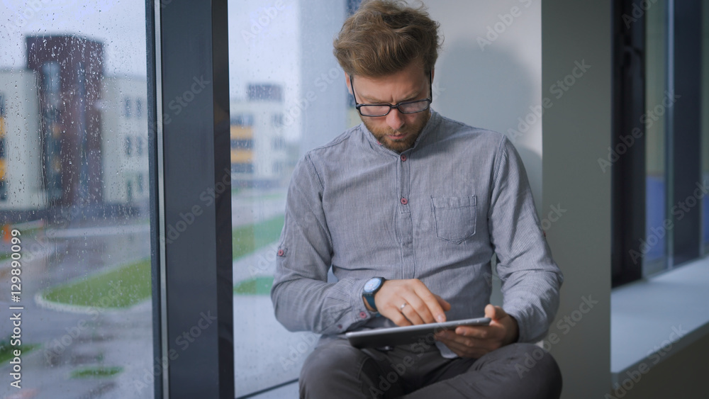 Fototapeta premium Young businessman is sitting at window and browsing